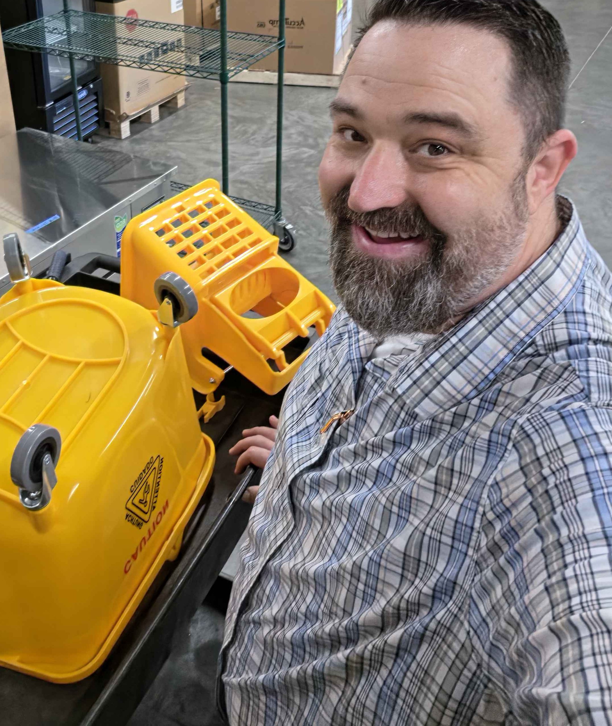 Dan Haefner smiling beside an upside-down yellow commercial mop bucket and wringer while installing its casters